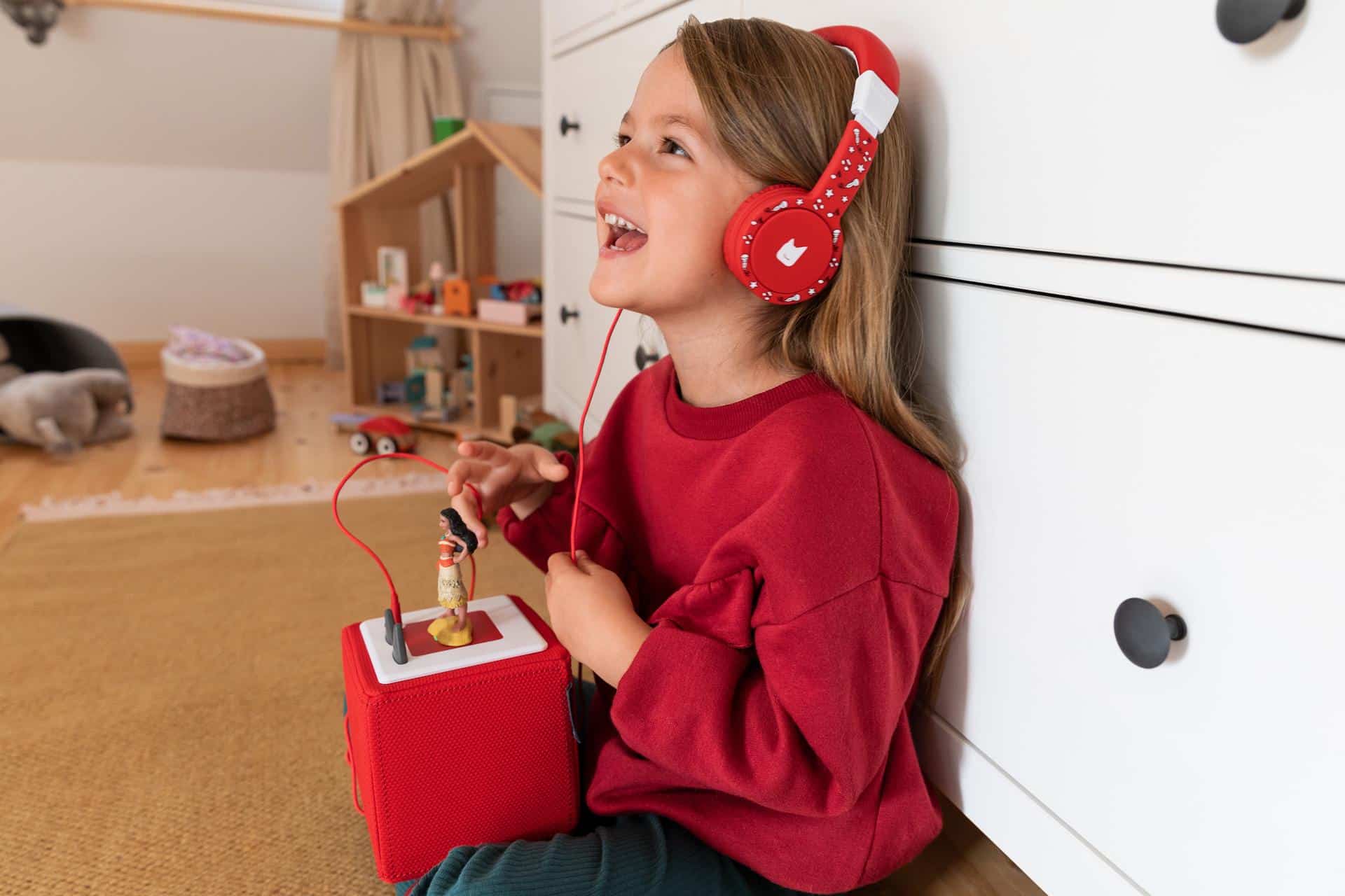 Une fillette est assise dans sa chambre et écoute de la musique sur son Toniebox avec des écouteurs.
