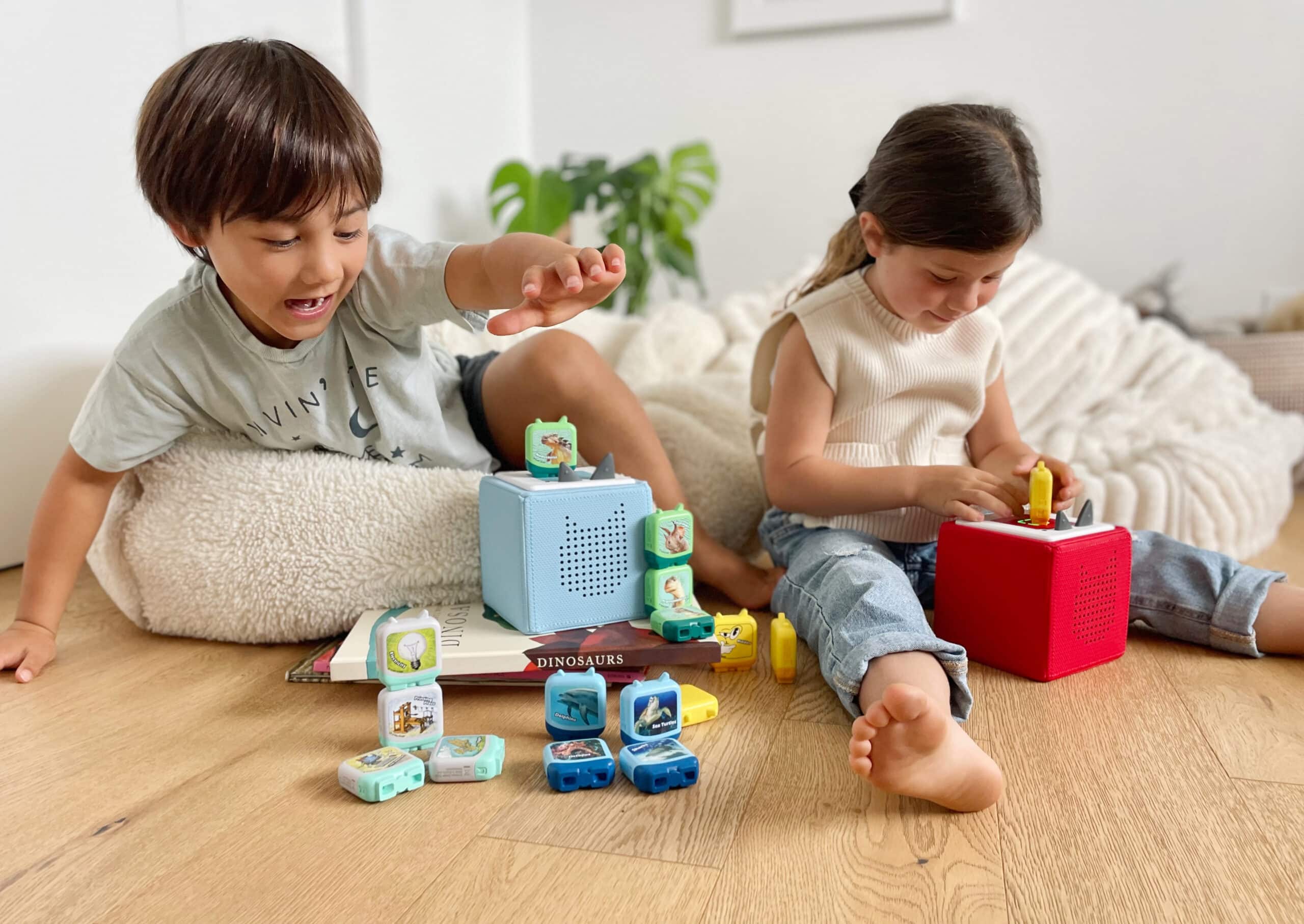 Deux enfants sont assis dans une chambre d'enfant et écoutent des Tonies sur leur Toniebox.