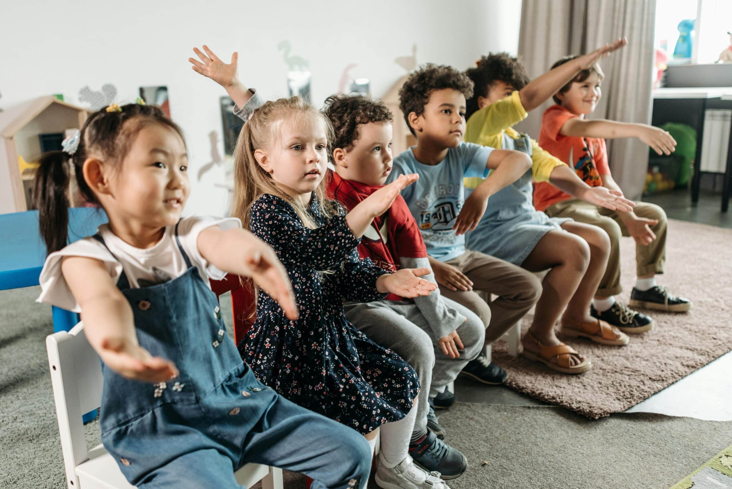 Les enfants jouent à un jeu participatif sur des chaises, où ils doivent bouger les bras.